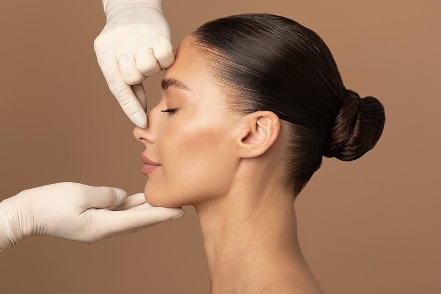 Plastic surgery and beauty concept. Surgeon touching woman nose, consulting before rhinoplasty operation on brown background, side view